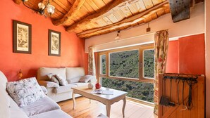 Una habitació acollidora amb sostre de fusta, un sofà, una taula i una finestra que dona a un bosc.
