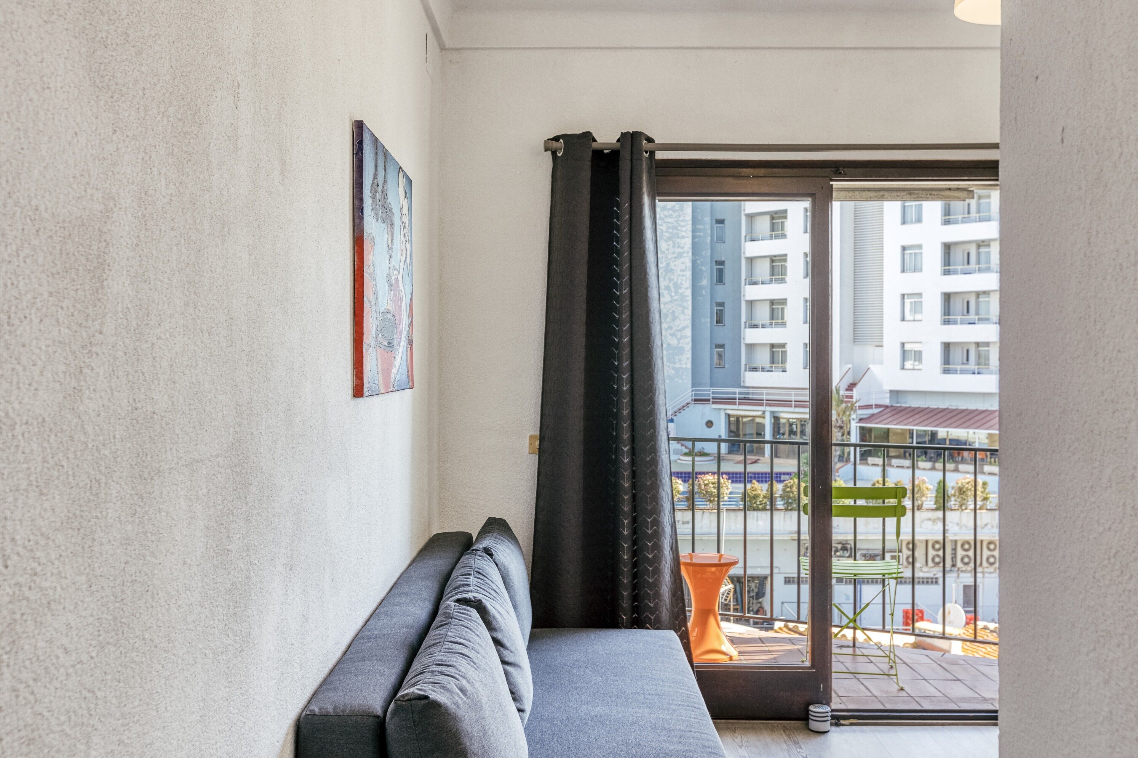 Ein Balkon mit einer Couch, einem Bild an der Wand und Blick auf ein Gebäude.