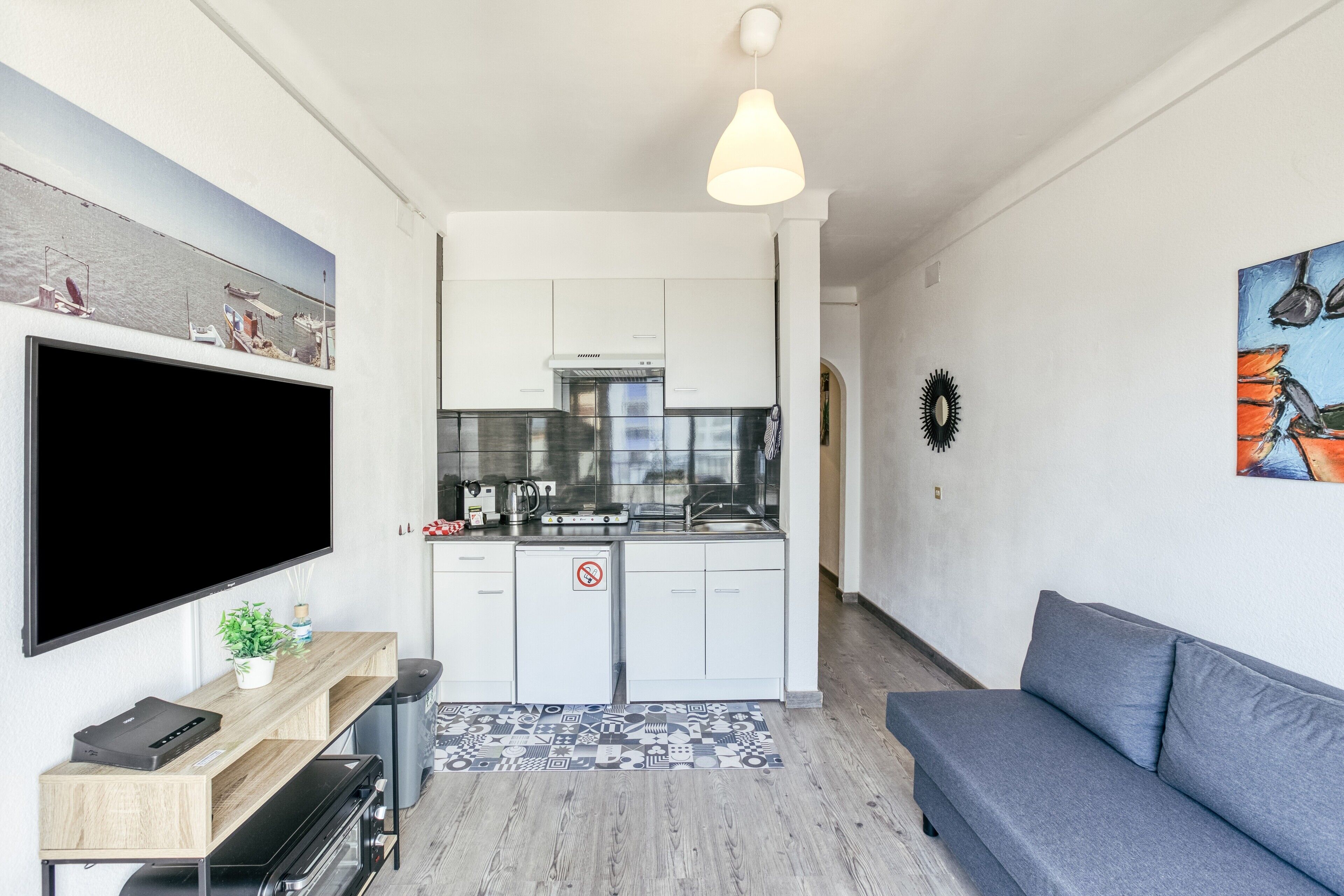 A compact living space with a kitchenette, a flat-screen TV, a sofa, and a patterned rug.