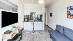 A compact living space with a kitchenette, a flat-screen TV, a sofa, and a patterned rug. - Apartment 'Casa Jois' with Sea View, Wi-Fi and Air Conditioning (Empuriabrava)