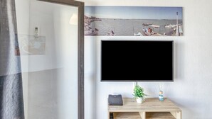 A room with a mounted TV, a wooden side table with a plant, and a framed picture of a beach scene. - Apartment 'Casa Jois' with Sea View, Wi-Fi and Air Conditioning (Empuriabrava)