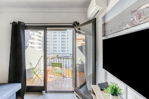 Un balcon donnant sur un immeuble, avec une chaise et une petite table sur laquelle est posée une plante.
