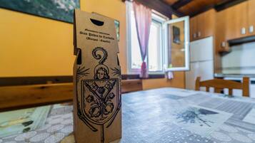 A table with a patterned tablecloth, a brown paper bag with a crest, and a window with curtains in the background.