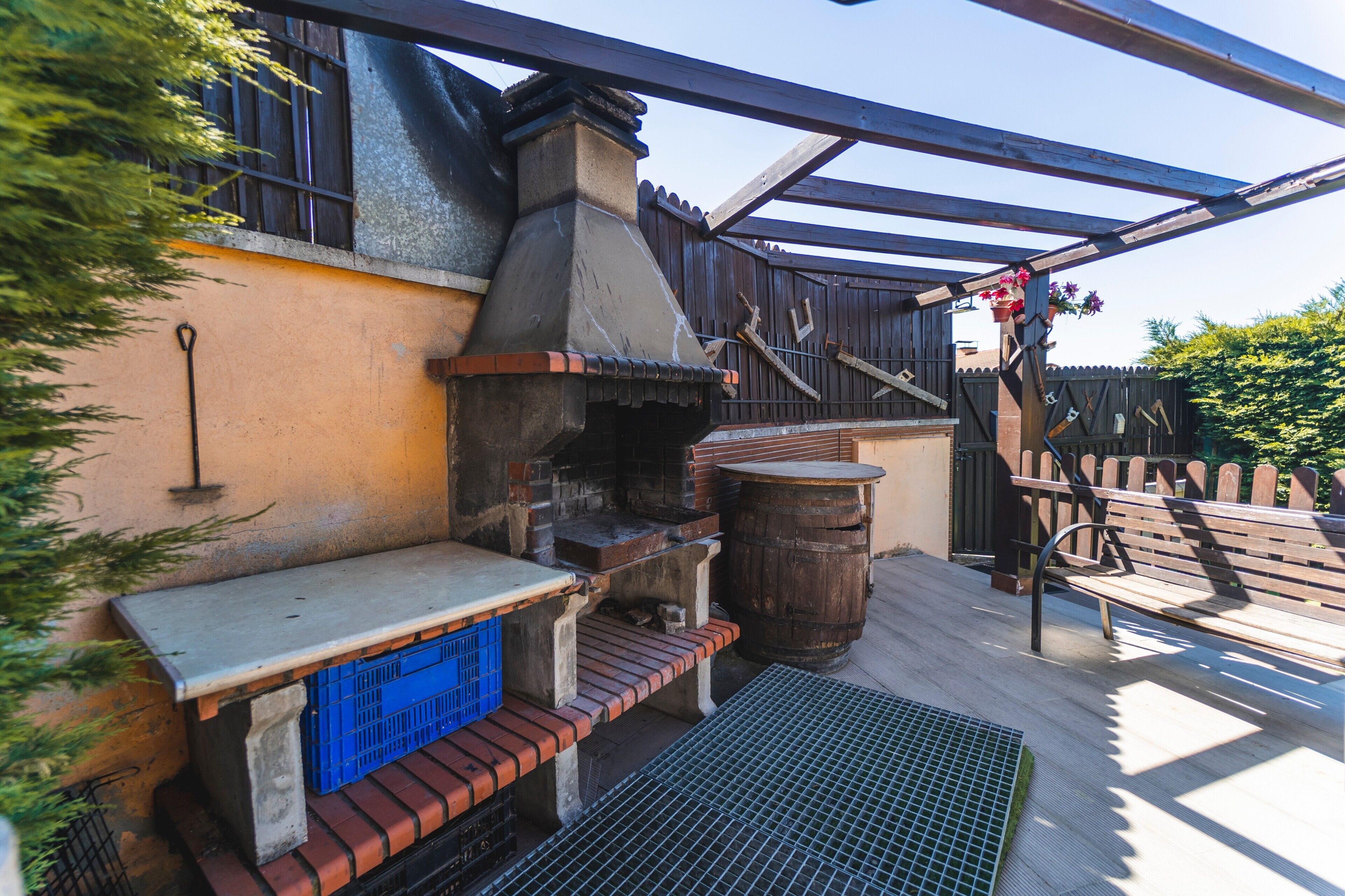 Une terrasse extérieure avec un espace barbecue en briques, un banc en bois et un gril en métal.