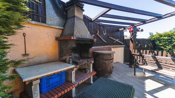 Une terrasse extérieure avec un espace barbecue en briques, un banc en bois et un gril en métal.