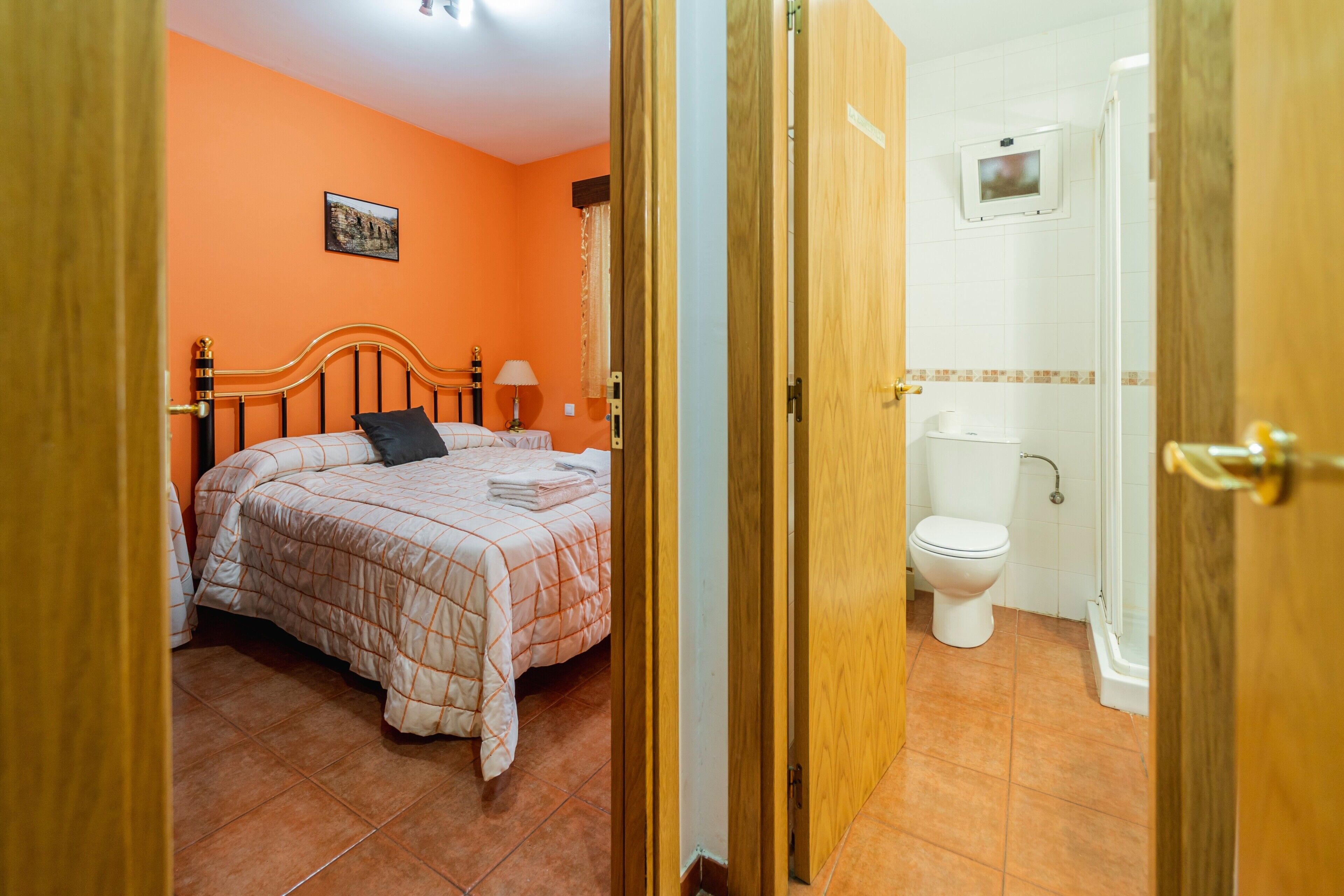 Een slaapkamer met een bed, nachtkastje, lamp en een badkamer met toilet en douche.