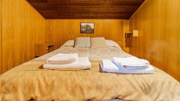 Habitació amb parets de fusta, un llit amb edredó beix, dos coixins i tovalloles doblegades.