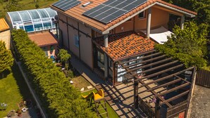 Une maison dotée d’une grande véranda en verre, de panneaux solaires, d’une terrasse en bois et d’un jardin clôturé.