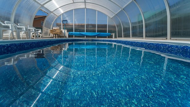 Une piscine d ’un bleu éclatant, surmontée d’un toit de verre, entourée de chaises blanches et d’une serviette bleue.