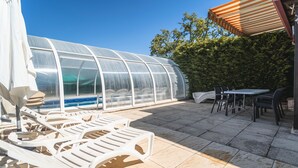 Une terrasse avec des chaises longues, une table et une structure de serre.