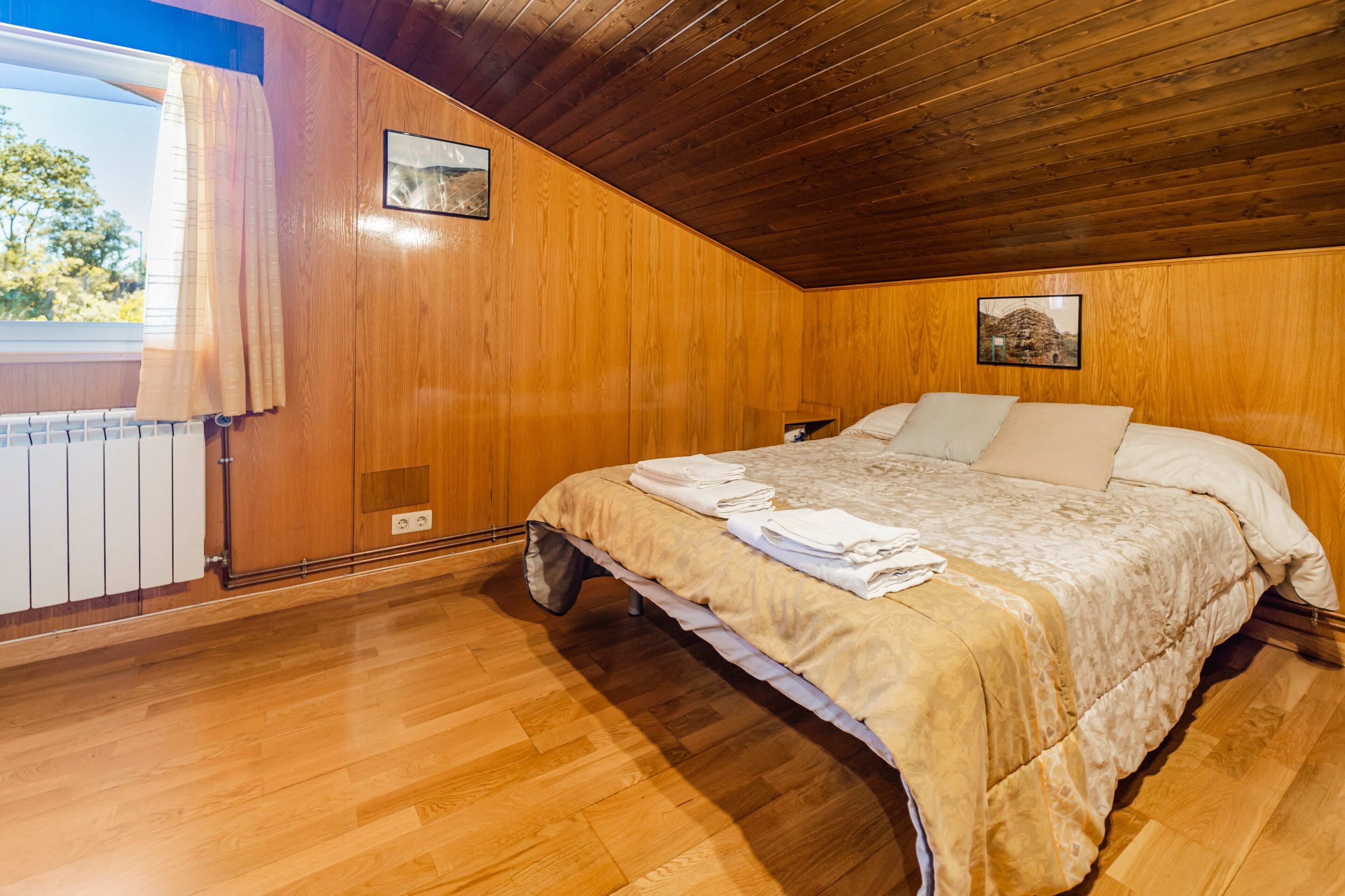Una camera da letto con pareti in legno, un letto con copripiumino beige e due quadri appesi.