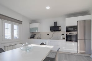 A modern kitchen with white cabinetry, a stainless steel refrigerator, a Bosch oven, and a dining table with a glass cake stand. - Holiday Home 'A Neida Con Vistas Al Mar' with Sea View, Private Terrace and Wi-Fi (Cee)