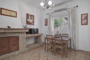 A dining area with a brick fireplace, a table with chairs, and a window with curtains.