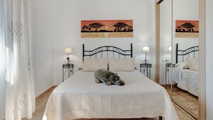 A bedroom with a bed, two bedside tables with lamps, a mirror, and two wall paintings. - Holiday Home 'Villa Sheyla Maria' with Private Pool, Private Terrace and Air Conditioning (Conil de la frontera)