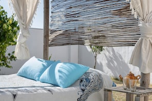 A bed with blue pillows, a patterned bedspread, a wicker headboard, and a small table with a teapot and glasses.