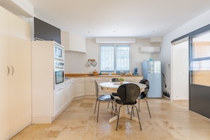 A modern kitchen with white cabinetry, a dining table with chairs, a refrigerator, and a window with blinds.