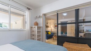 A bedroom with a bed, a wicker basket, a blue sofa, and a kitchen area visible through a glass door. - Apartment 'Lobéal' with Shared Pool, Wi-Fi and Air Conditioning (Auriol)