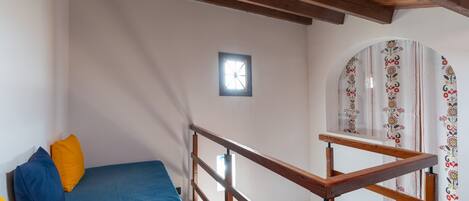 Una habitación con cama, vigas de madera en el techo, una ventana pequeña y una cortina estampada.