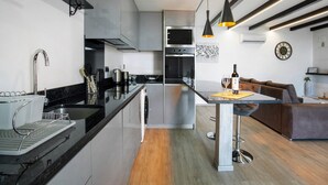 A modern kitchen with a central island, stainless steel appliances, and a dining area with a sofa and table. - Holiday Home 'Refugio Do Lourinho' with Sea View, Wi-Fi and Air Conditioning (Calheta)