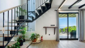 A staircase with black railings, a fire extinguisher, potted plants, and a view through a glass door to an outdoor seating area. - Holiday Home 'Refugio Do Lourinho' with Sea View, Wi-Fi and Air Conditioning (Calheta)