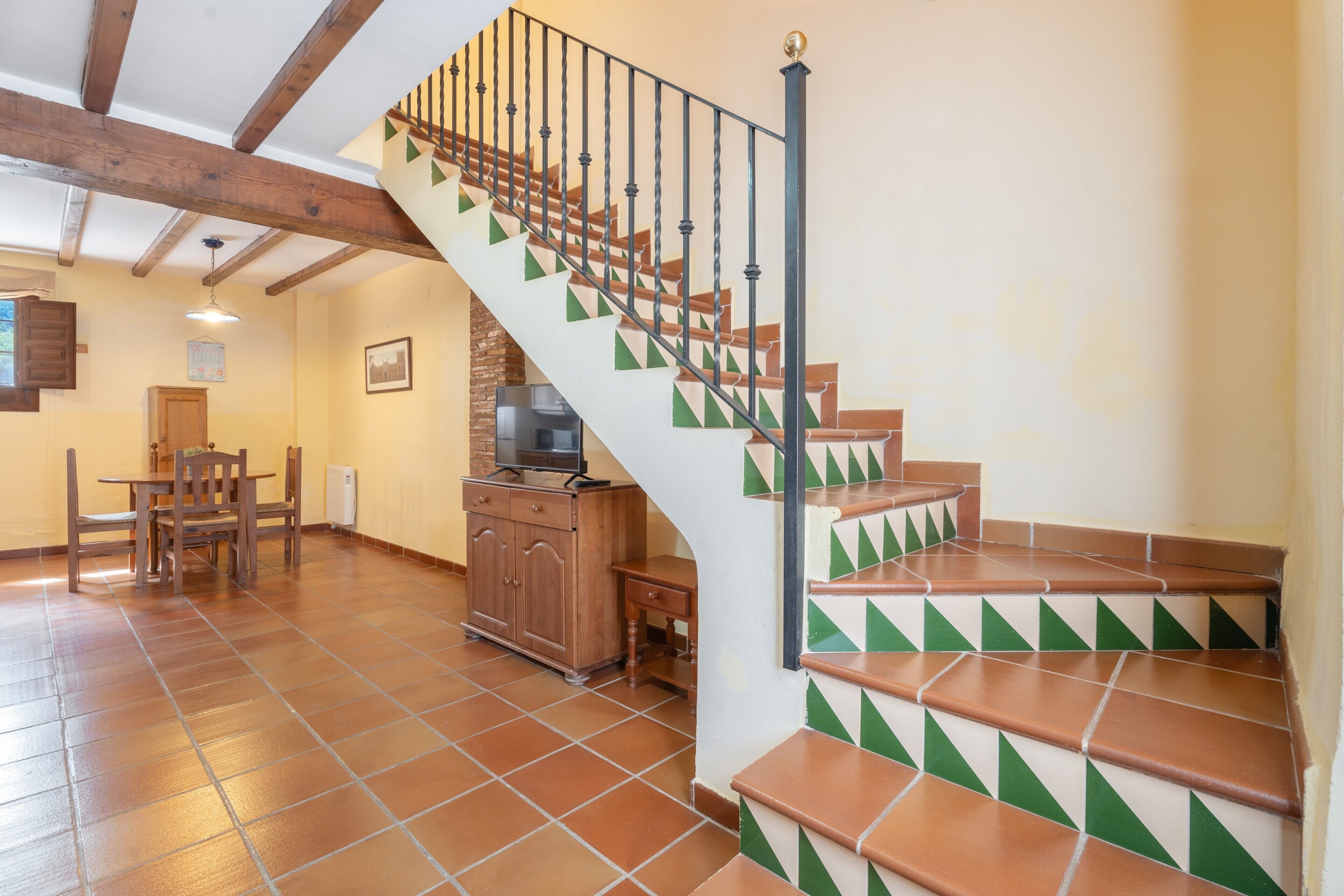 A staircase with green and brown tiles, wooden beams, and a dining area with a table and chairs.