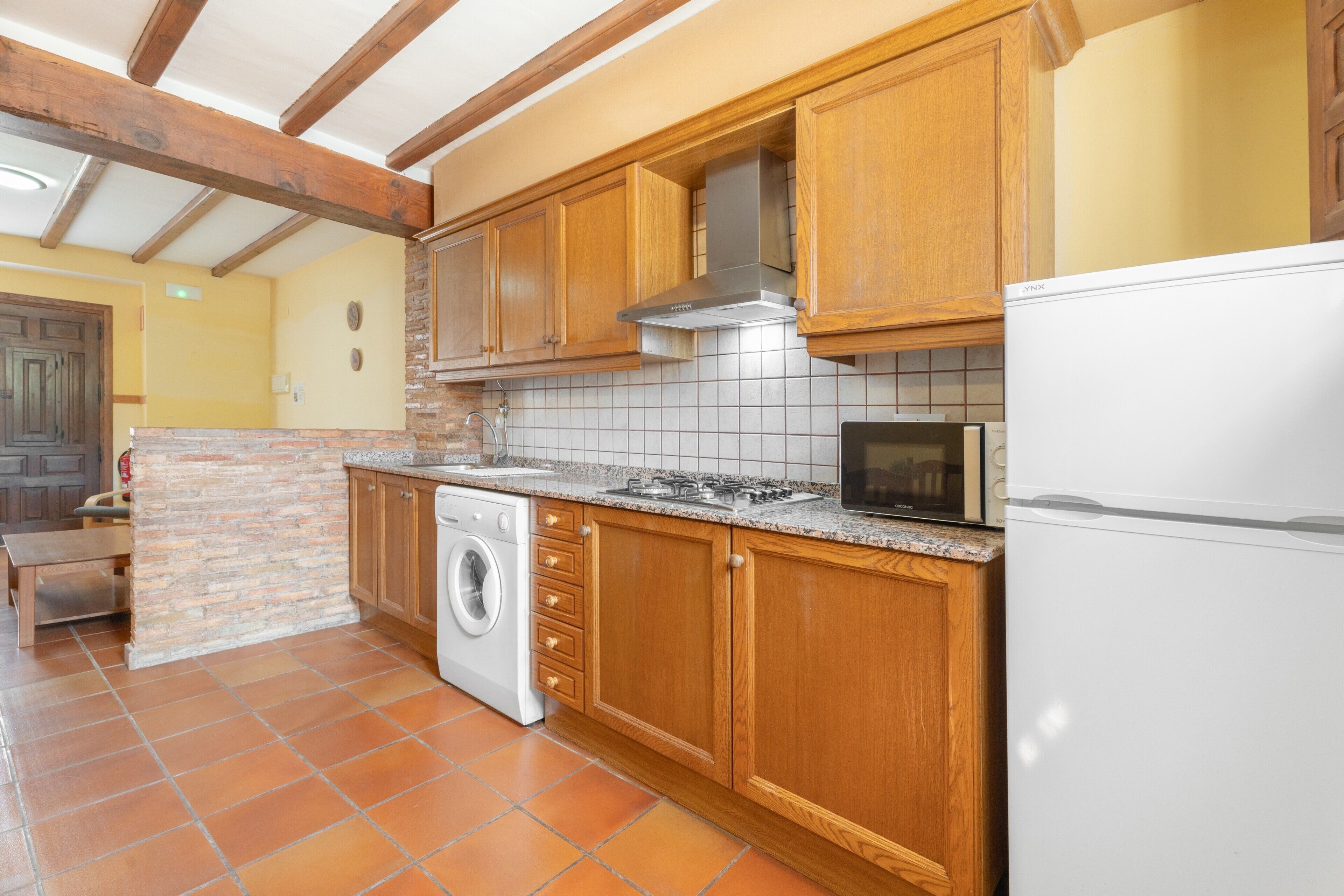 Une cuisine avec des meubles de rangement en bois, un lave-linge, un four à micro-ondes et un réfrigérateur.