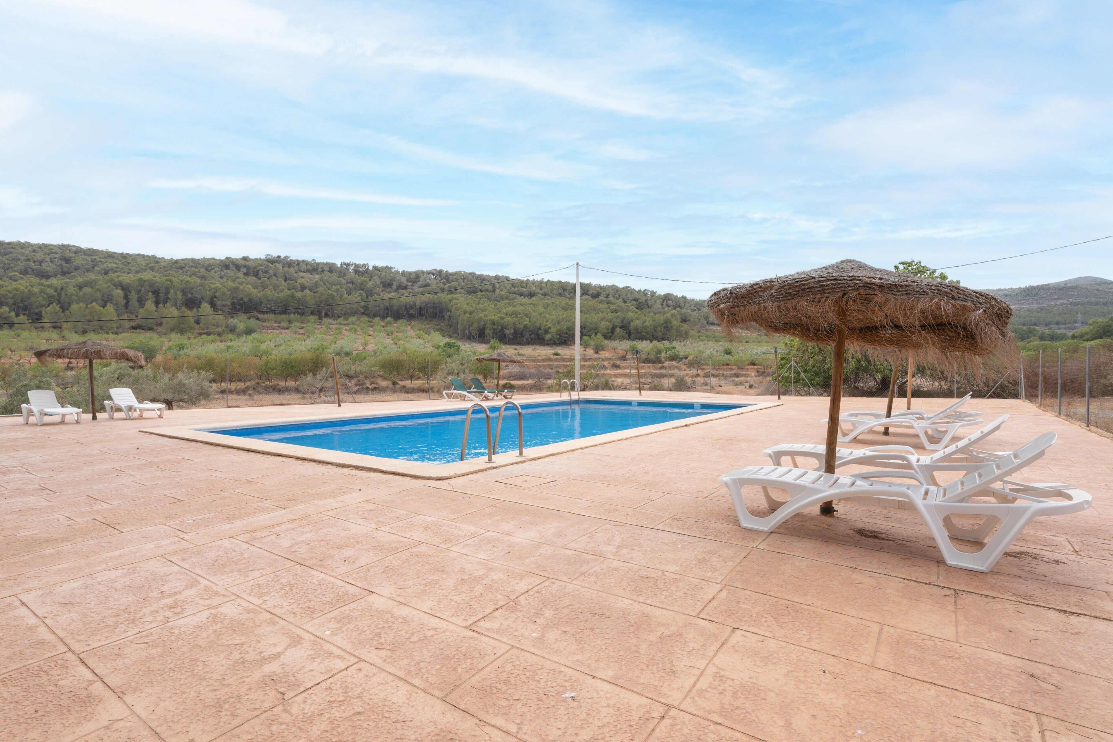 A swimming pool with lounge chairs and a thatched umbrella.
