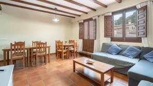 Una sala de estar con un sofá, una mesa de comedor con sillas, una mesa de centro de madera y una ventana con contraventanas.