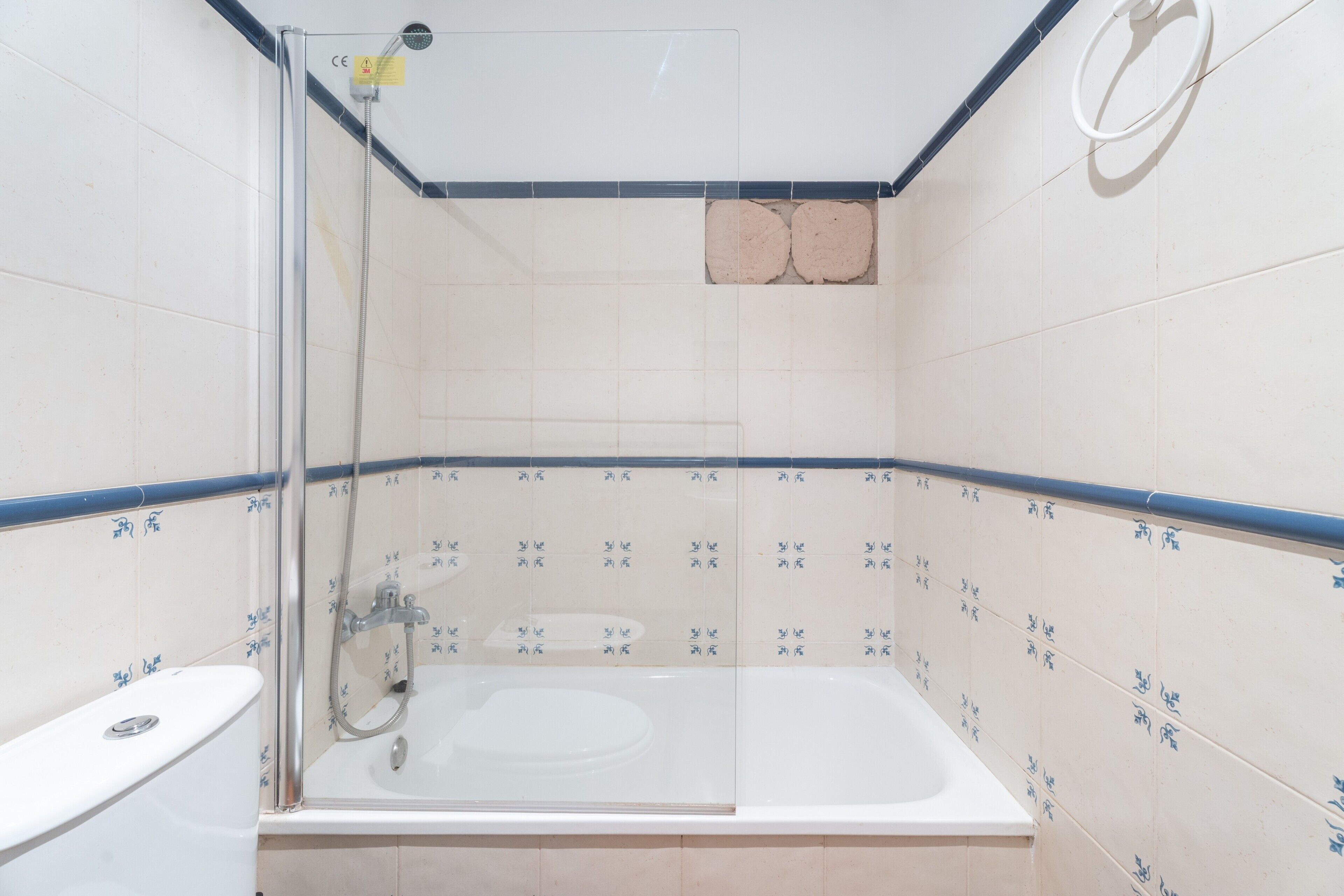 Un baño con ducha de vidrio, una bañera blanca y paredes de azulejos con diseños azules.