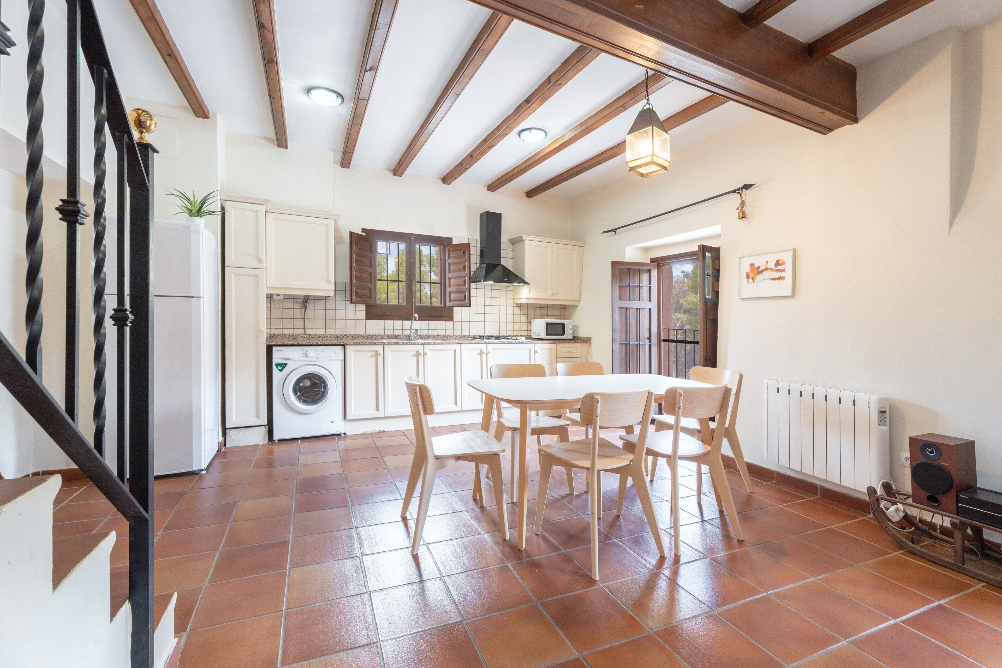 Una cocina con armarios blancos, una mesa de comedor con sillas, una lavadora y un radiador.