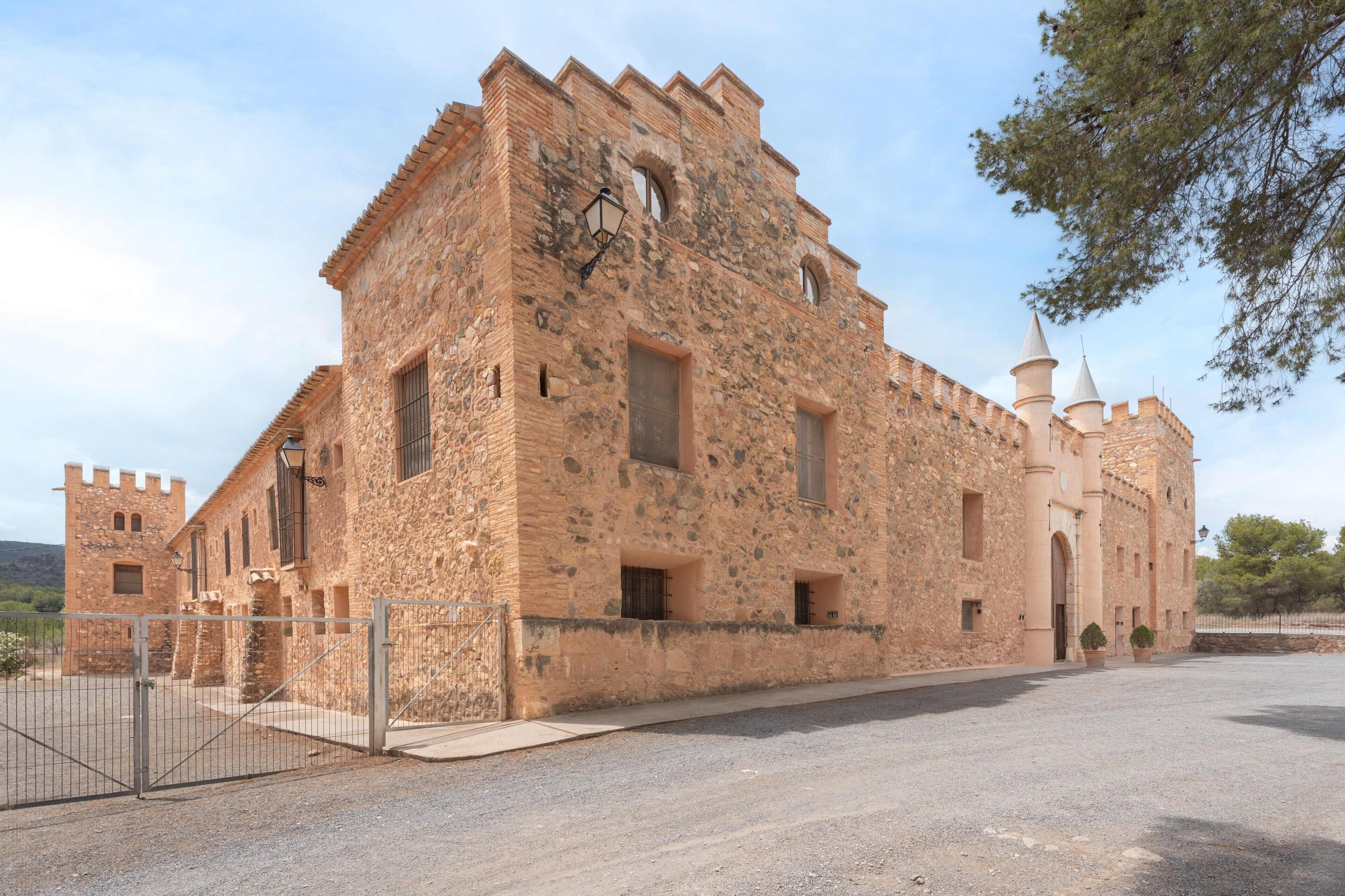A historic stone building with a tower, a gated entrance, and a paved courtyard.