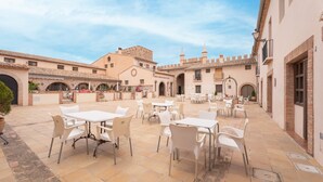 A courtyard with outdoor seating, a fountain, and a building with a tiled roof.
