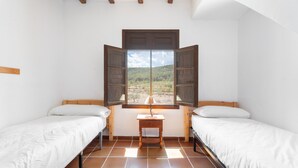A room with two beds, a small table, and a window with open shutters.