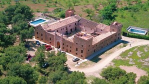 An aerial view of a large, historic building with multiple rooms, a swimming pool, and a tennis court.