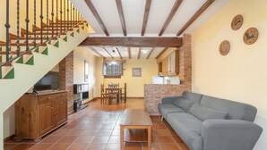 Amplia sala de estar con escaleras, muebles de madera y una cocina al fondo.