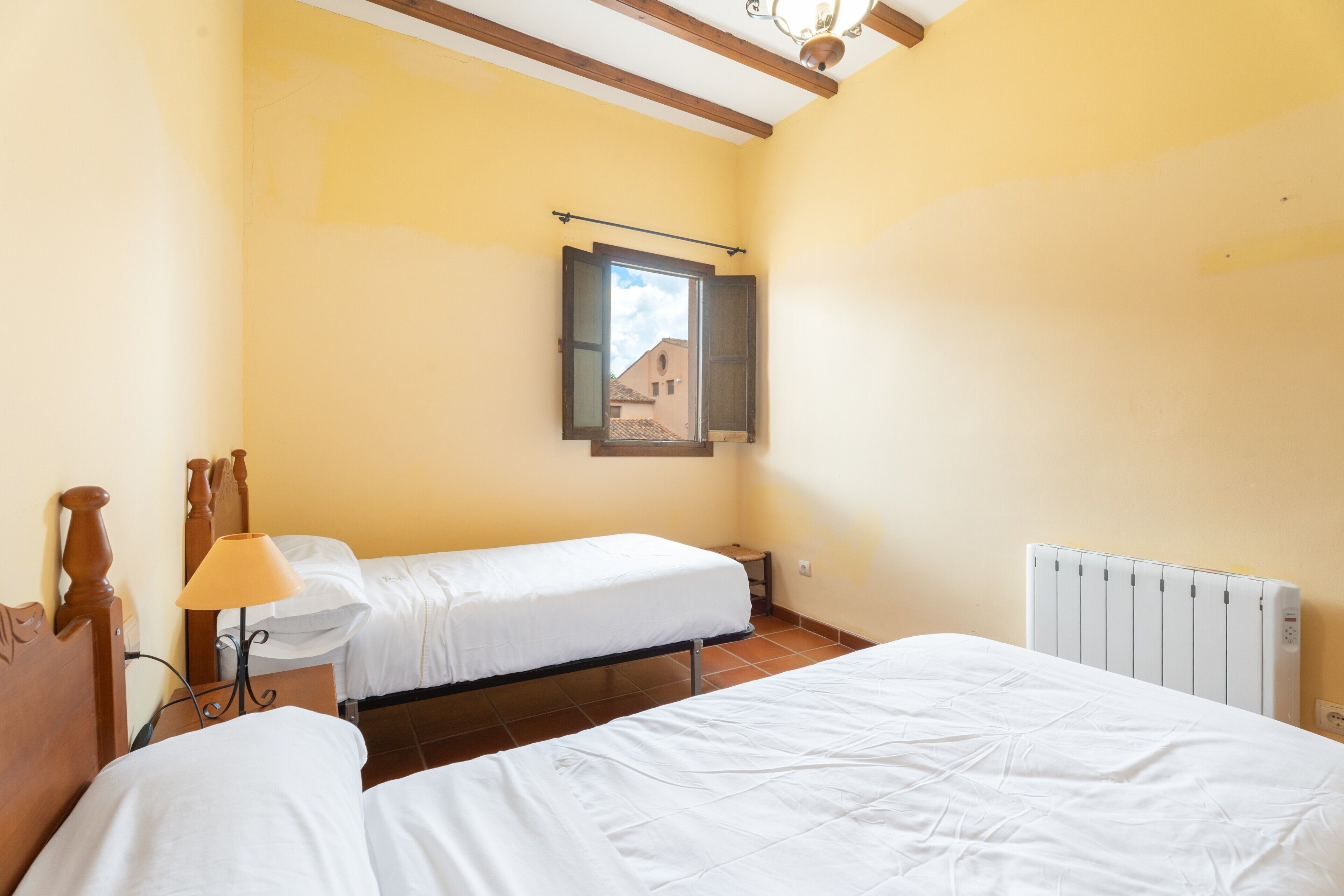 A bedroom with two beds, a window with a view, a lamp, and a radiator.