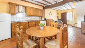 Una cocina con armarios de madera, un refrigerador blanco, una mesa de comedor con sillas, una planta en maceta y un salpicadero de azulejos.
