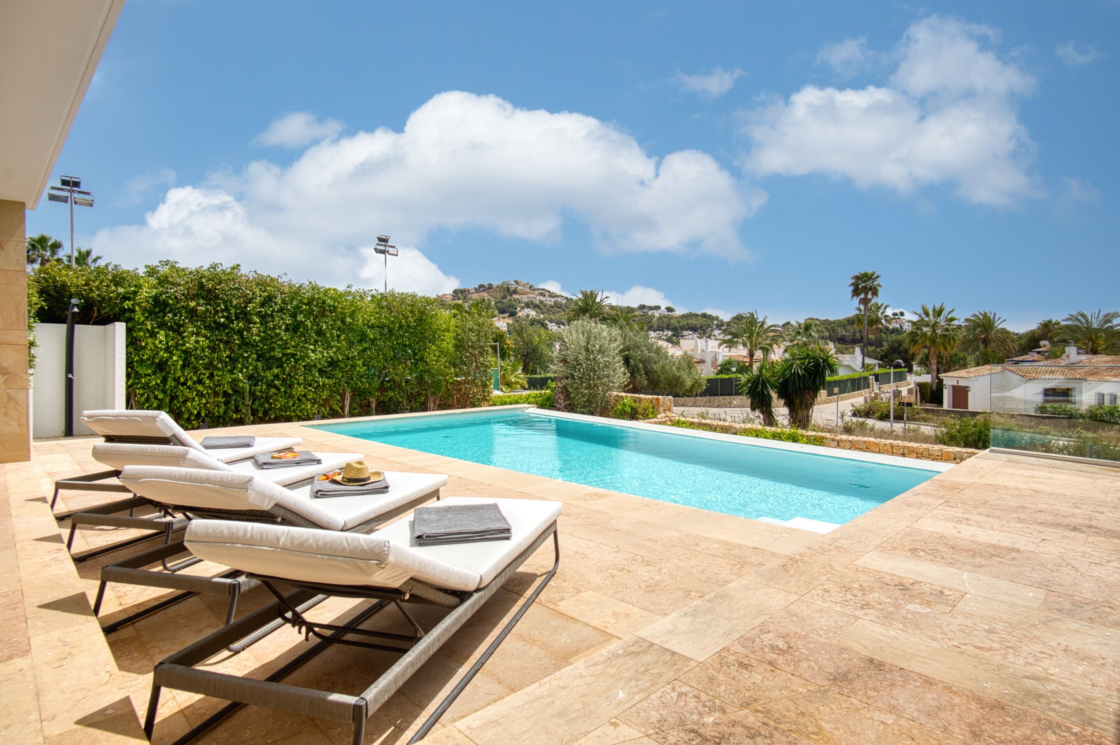 A pool area with lounge chairs, a clear blue sky, and a view of a hilly landscape.