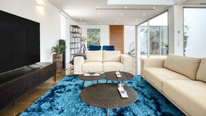 A modern living room with a large flat-screen TV, a beige sofa, two round coffee tables, and a blue shag rug. - Villa 'Azul' with Mountain View, Wi-Fi and Air Conditioning (Teulada)
