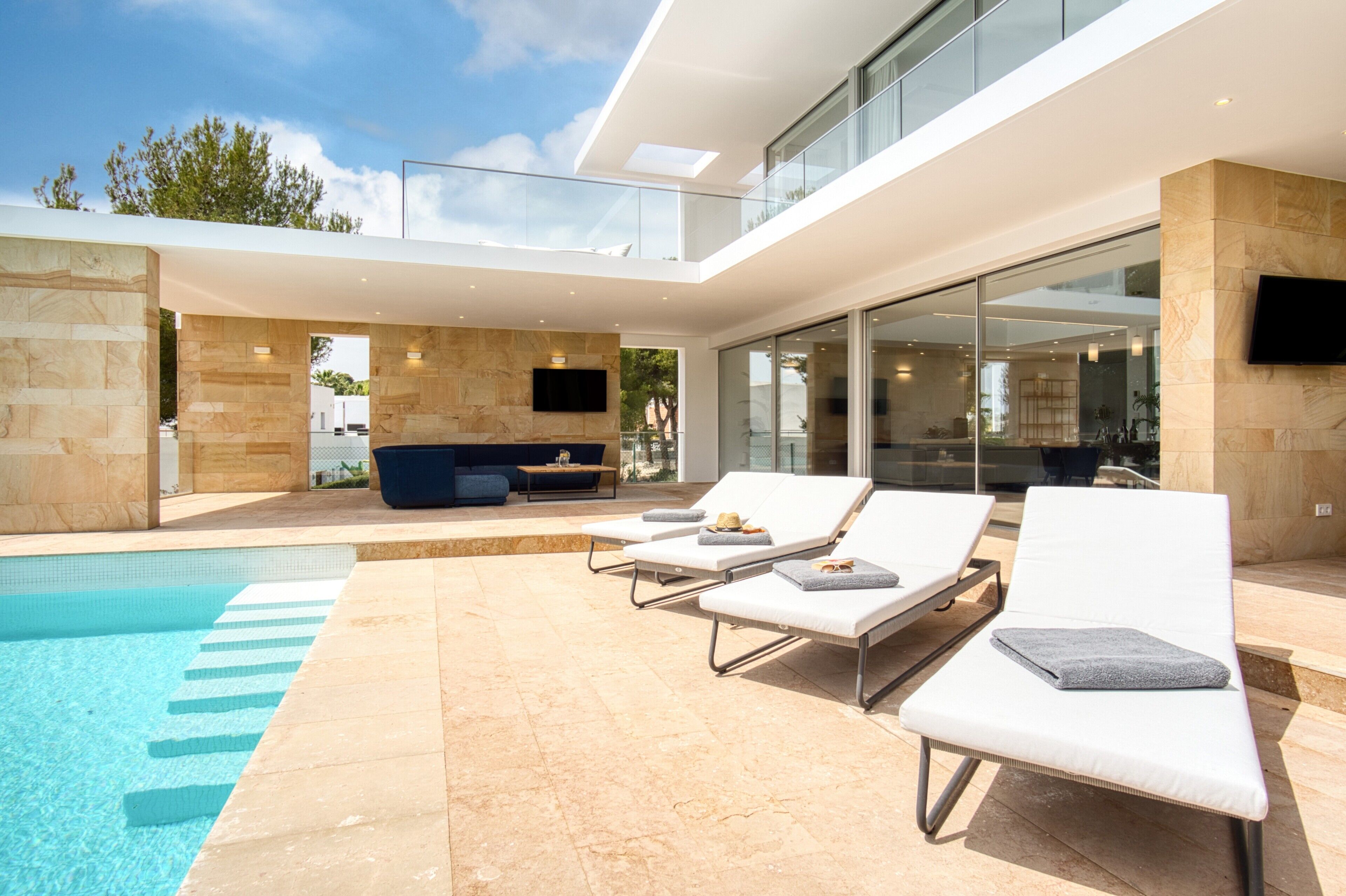 A modern outdoor pool area with lounge chairs, a seating area, and a flat-screen TV mounted on the wall.