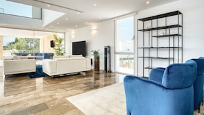 A modern living room with a sofa, a blue armchair, a TV, and a bookshelf. - Villa 'Azul' with Mountain View, Wi-Fi and Air Conditioning (Teulada)