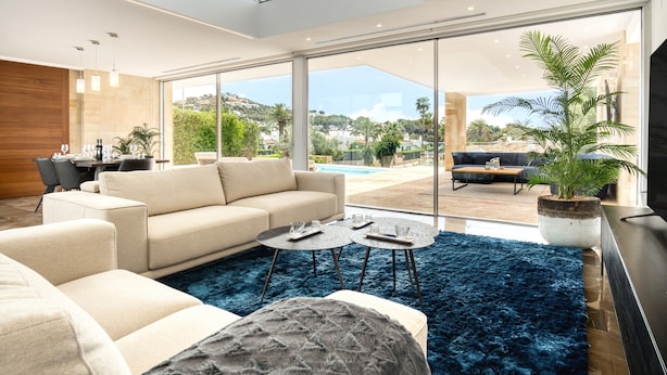A modern living room with a sofa, coffee table, and a large window offering a view of a pool and outdoor seating. - Villa 'Azul' with Mountain View, Wi-Fi and Air Conditioning (Teulada)