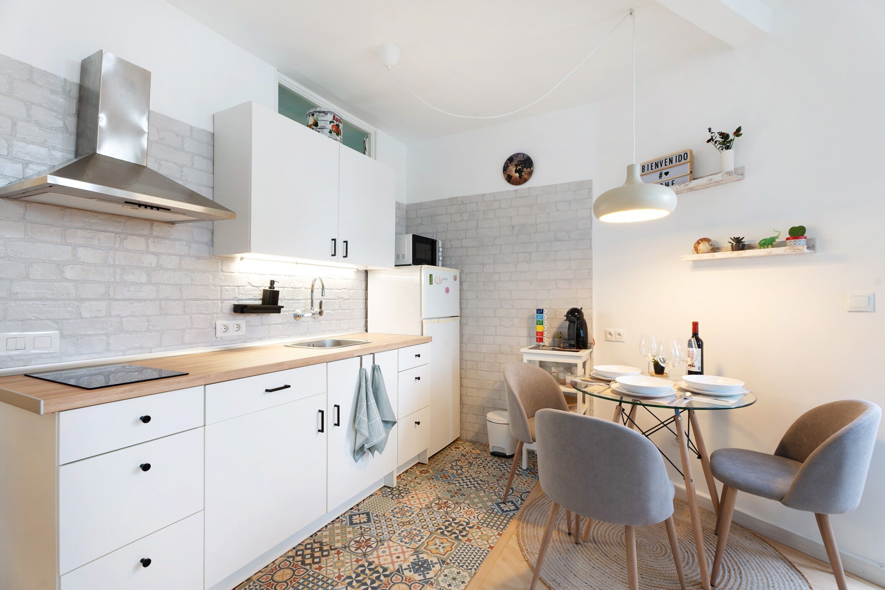 Una cucina moderna con mobili bianchi, una cappa aspirante in acciaio inossidabile, un forno a microonde e un'area pranzo con un tavolo in vetro e due sedie.