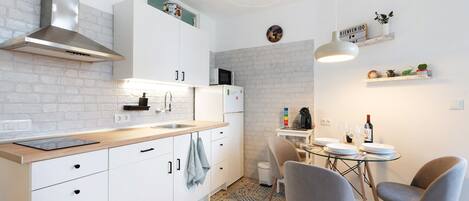 Una cucina moderna con mobili bianchi, una cappa aspirante in acciaio inossidabile, un forno a microonde e un'area pranzo con un tavolo in vetro e due sedie.