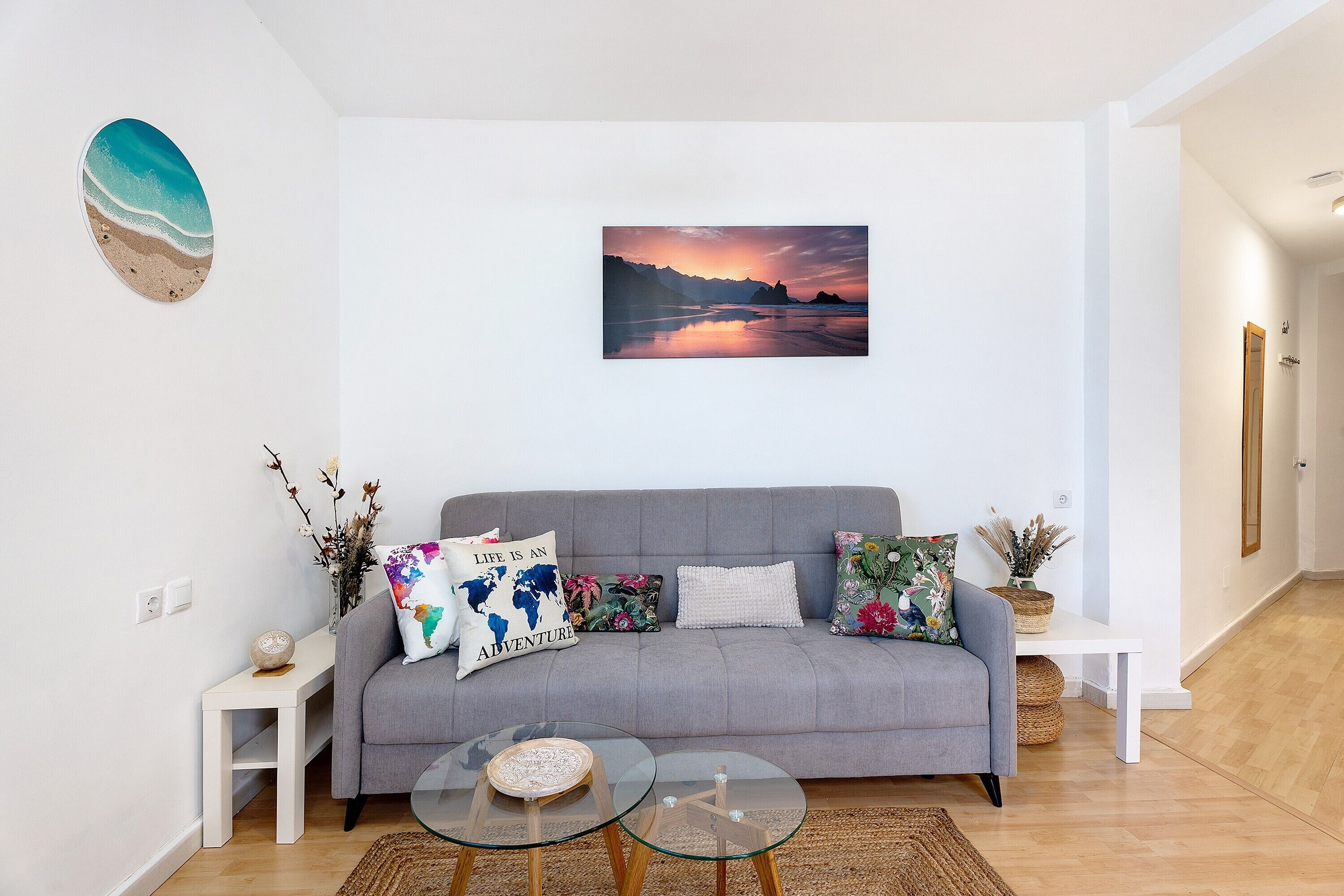 Una sala de estar moderna con un sofá gris, una mesa de centro de vidrio y un cuadro enmarcado con un paisaje.
