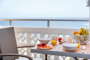 Une table de petit-déjeuner avec des fruits, du jus et un bol, placée sur un balcon donnant sur la mer.