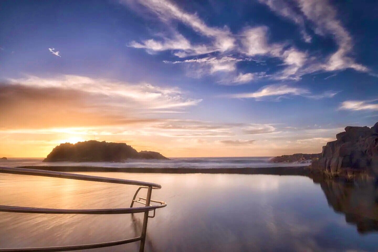Una escena costera tranquila con cielo despejado, aguas calmadas y formaciones rocosas.
