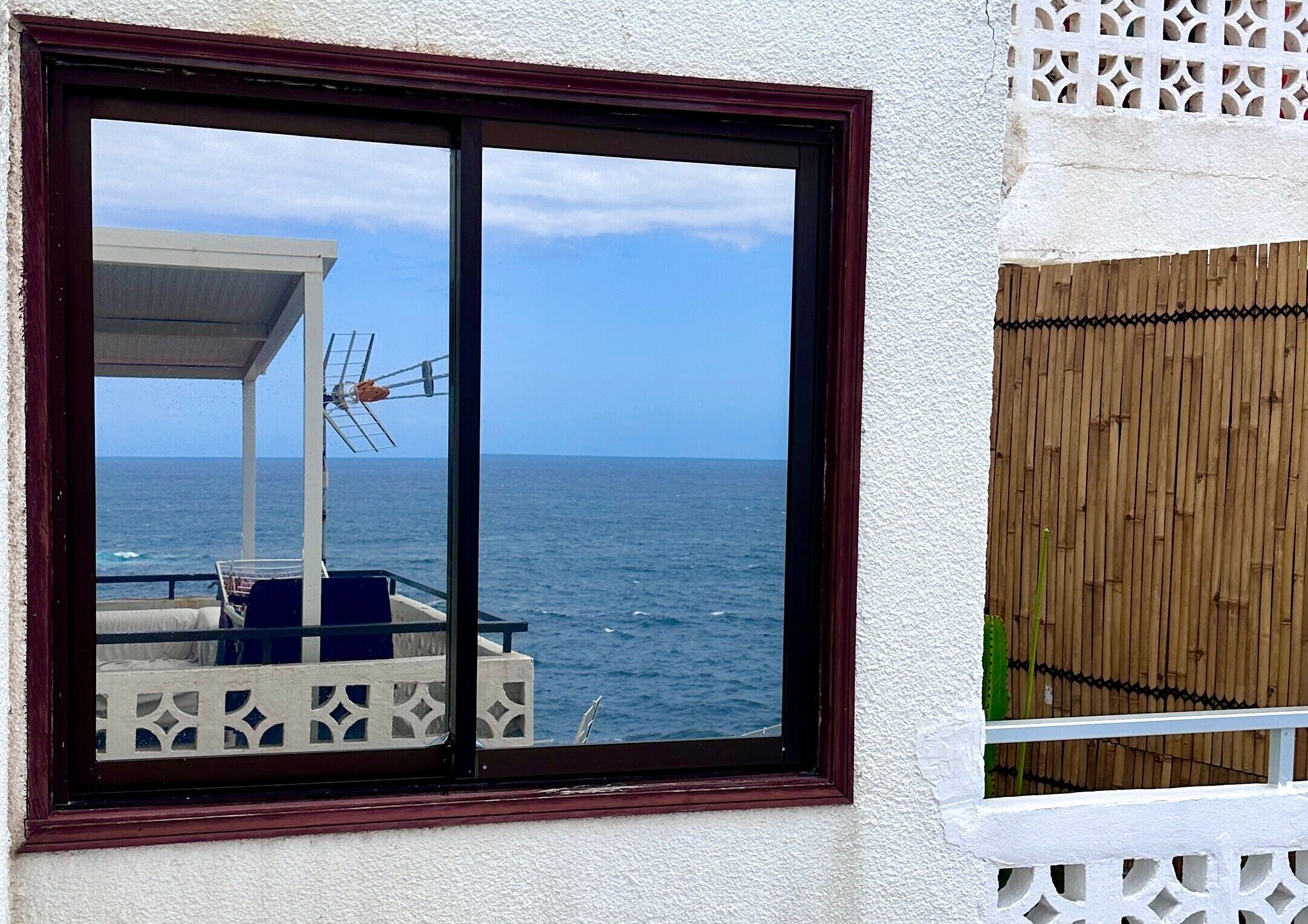 Ein Fenster mit Meerblick, eine überdachte Außenbereich-Sitzgelegenheit und ein Bambuszaun.