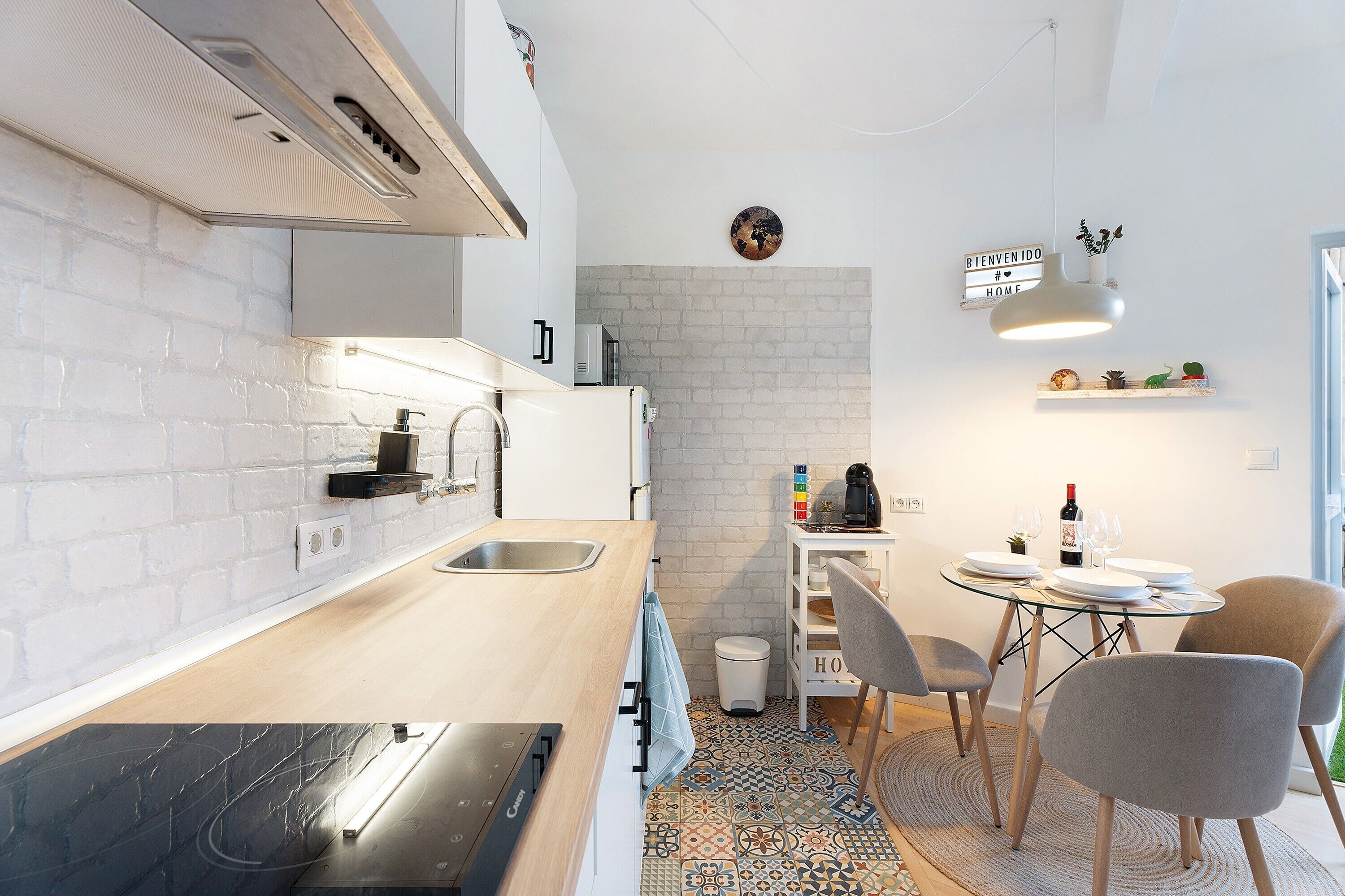 Een moderne keuken met een witte bakstenen spatwand, een ingebouwde oven en een eethoek met een ronde tafel en stoelen.