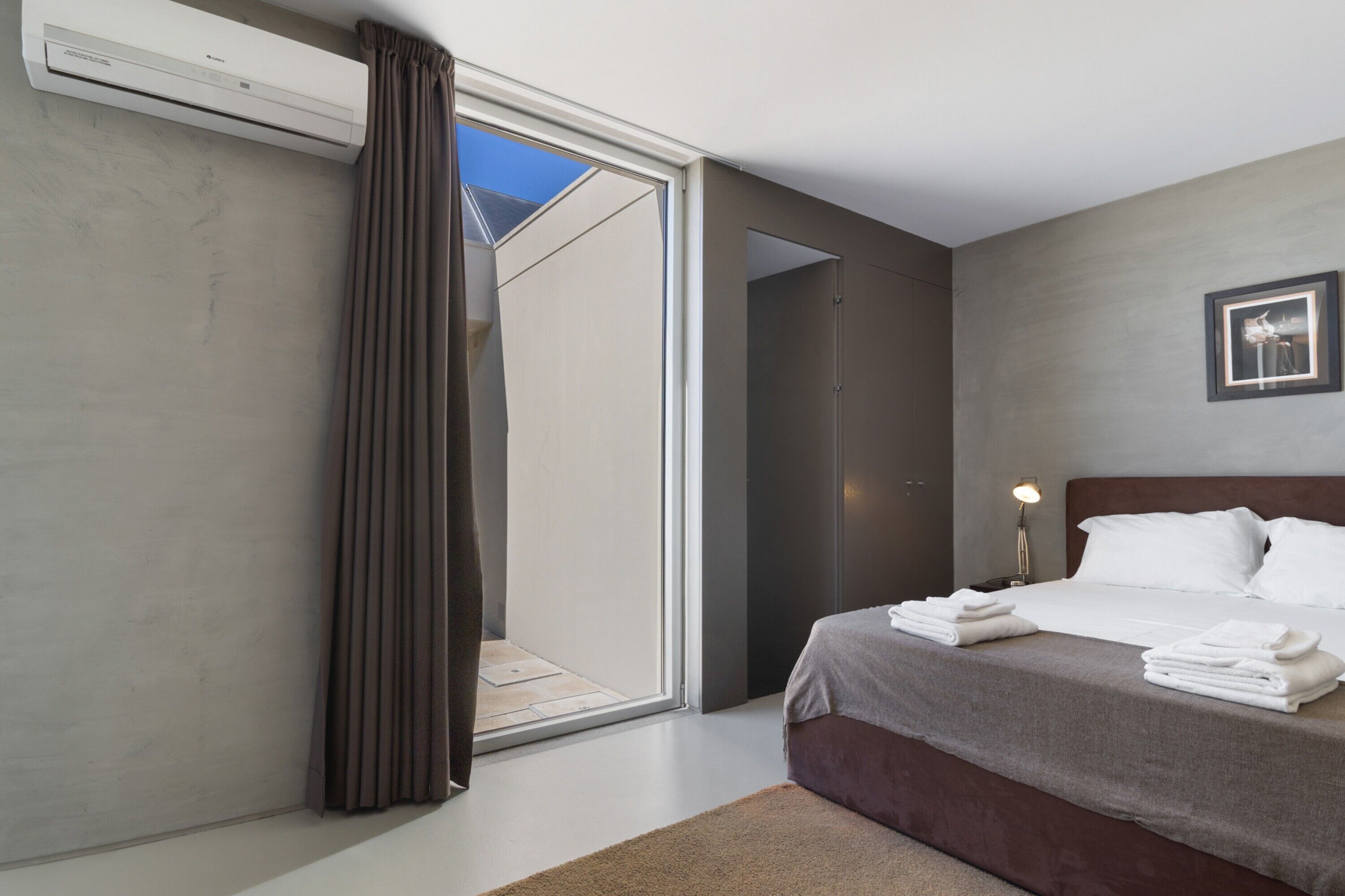 Une chambre d’hôtel moderne, équipée d’un lit, d’une table de chevet, d’un tableau encadré et offrant une vue à travers une porte coulissante.